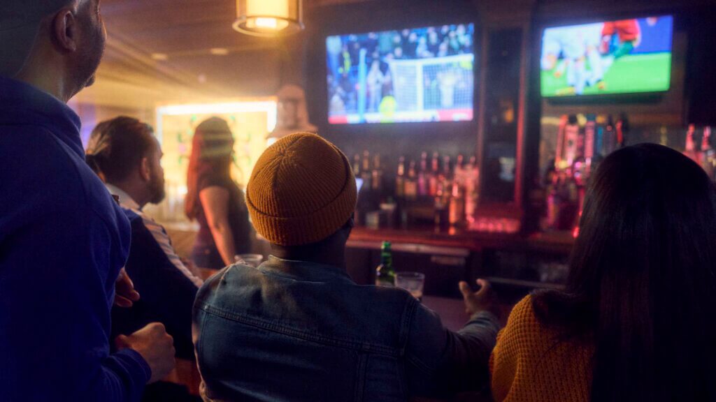 Friends Gathers Together At A Dimly Lit Bar To Watch A Soccer Gam