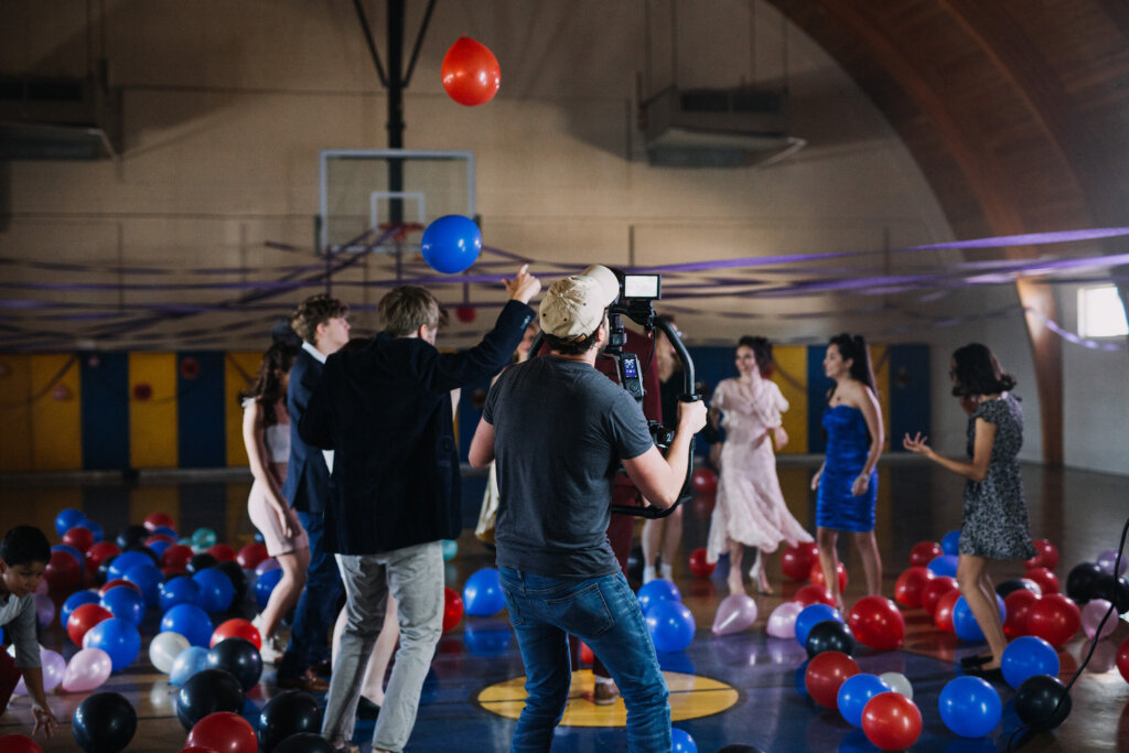 Jay Worsley filming with cast in gymnasium with balloons