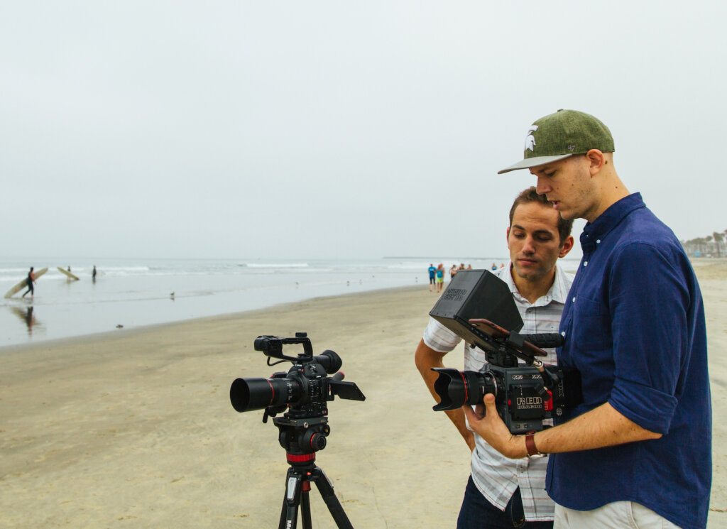 Caleb Wojcik filming on beach with crew member