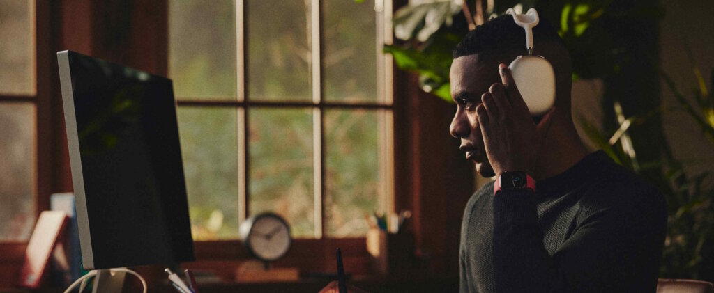 A Man In A Home Office, Wearing AirPods Max And Writing In A Notebook