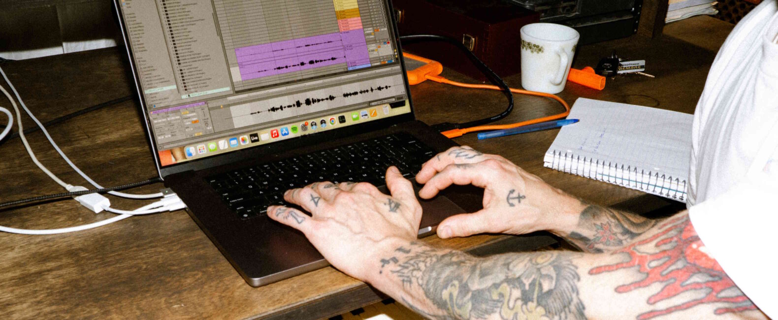 Person with tattooed arms typing on a laptop keyboard