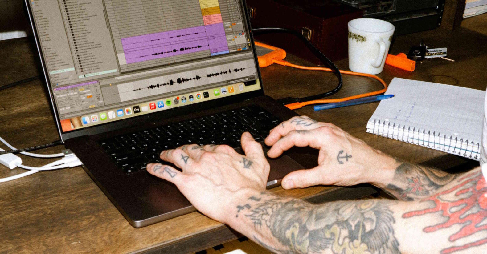 Person with tattooed arms typing on a laptop keyboard