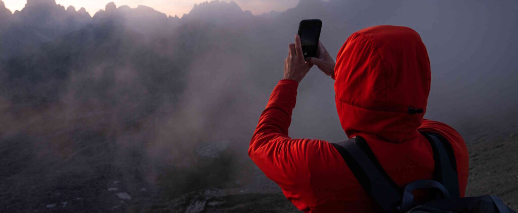 A person in a red coat and hood taking a photo with a smartphone.