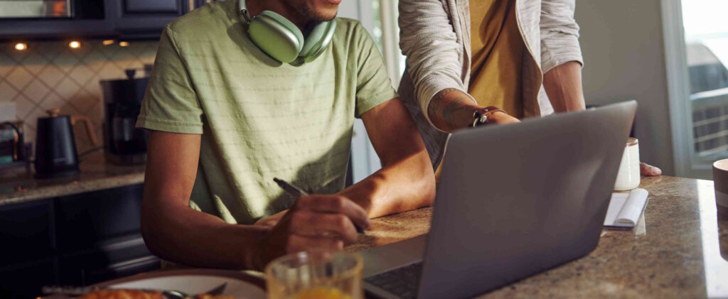 Young Man Sitting At The Kitchen Breakfast Table Looking At A Laptop