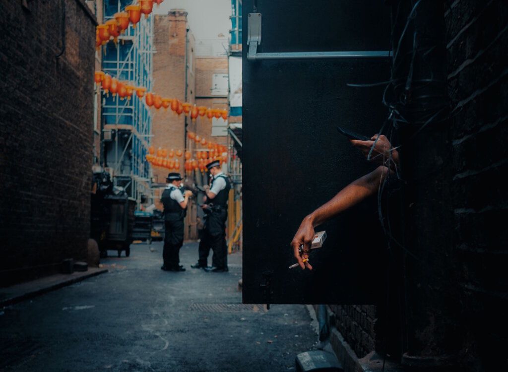 Person smoking and using their smartphone with police in the background