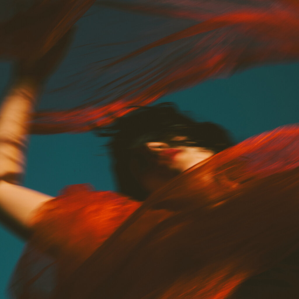 A Woman Holds Her Hands Against The Sky, Her Red Lips And Red Cloth A Stark Contrast Against The Blue