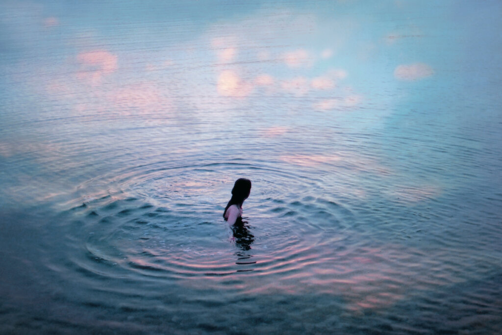 Someone Is Swimming In A Body Of Water Where The Clouds Are Reflecting On The Water