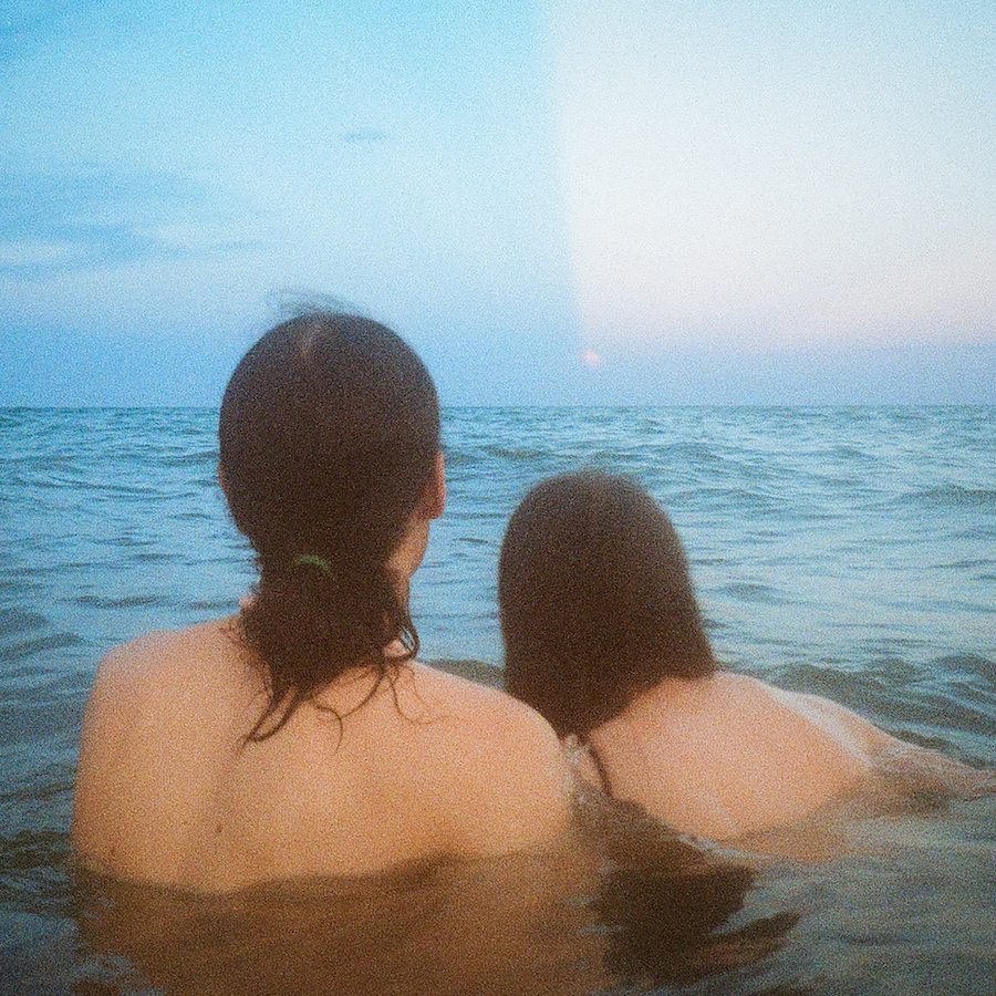 Man With Long Hair And Woman In Bikini Swim In Water Watching The Horizon