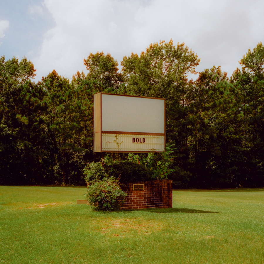 An Old Drive In Movie Marquee Sign In A Green Field With Trees Behind