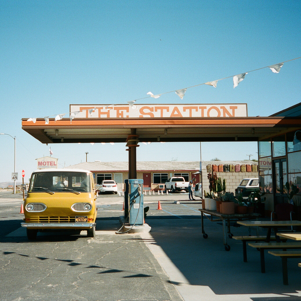 A Yellow Vintage Van Is Parked Outside Of A Gas Station