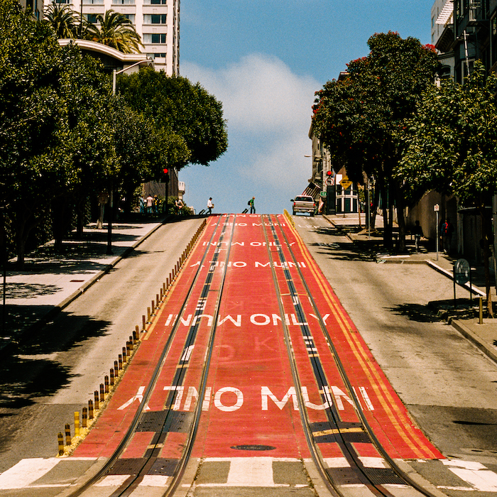 Train Tracks Cross A Zebra Crossing With People Crossing The Street In The Background