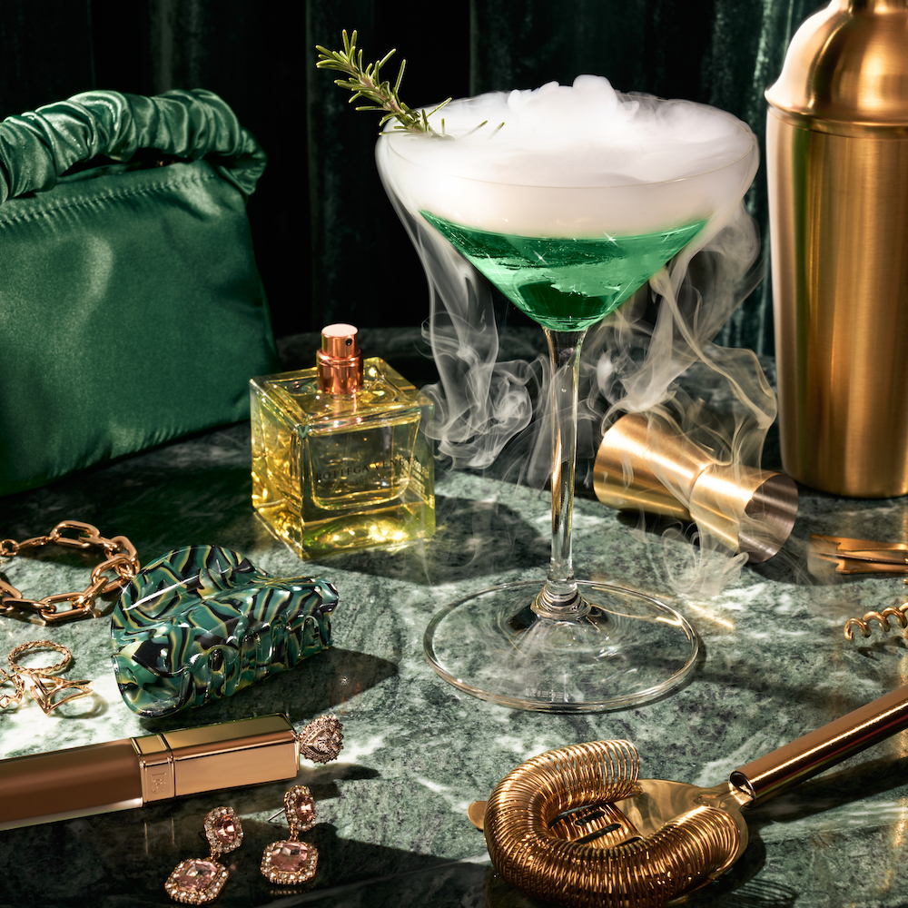 Greenish Cocktail In A Crystal Glass With Jeweled Handbags Around