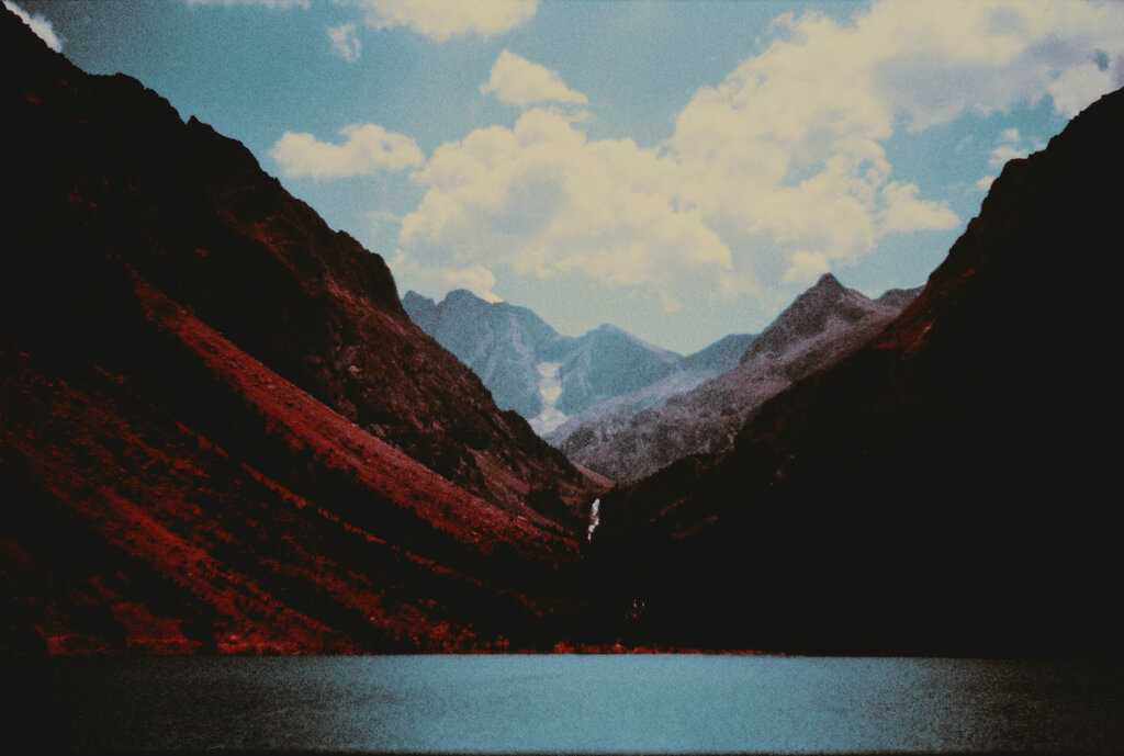 Mountain Rift Next To River With Other Mountains And Blue Sky
